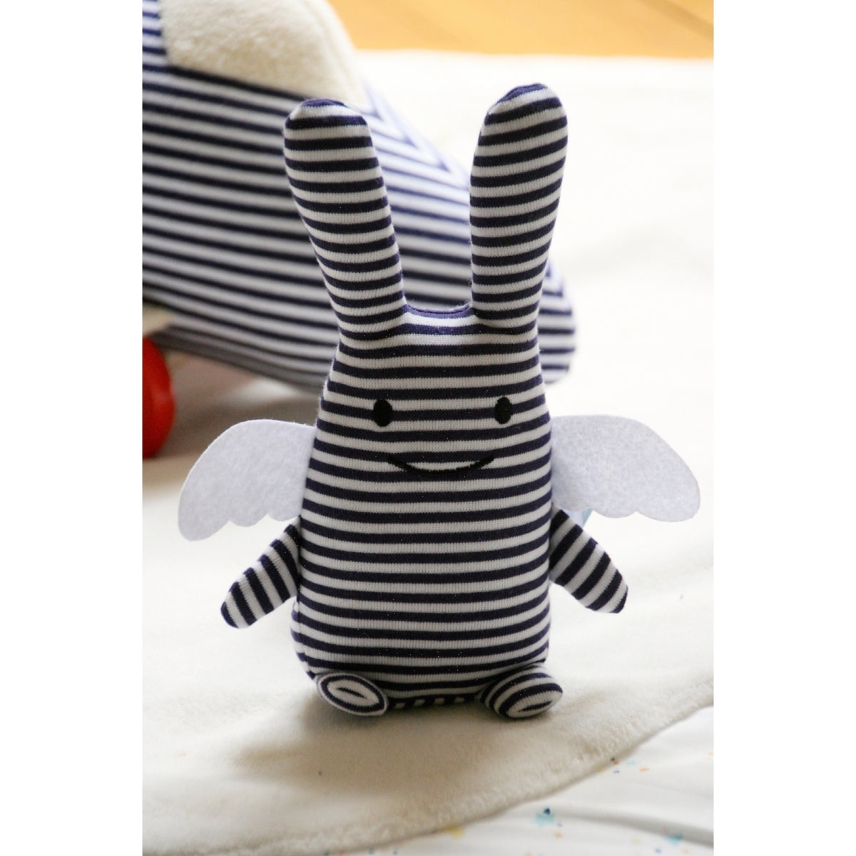 Doudou Ange Lapin avec hochet 20 cm — Trousselier — Marinière — mise en scène sur une couverture blanche 2 | Appart 17 Bruxelles