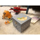 Boîte à musique cube Le Petit Prince Mouton, phosphorescente — Trousselier — Le Petit Prince — mise en scène sur un tapis, avec peluche renard et avion en bois 5 | Appart 17 Bruxelles